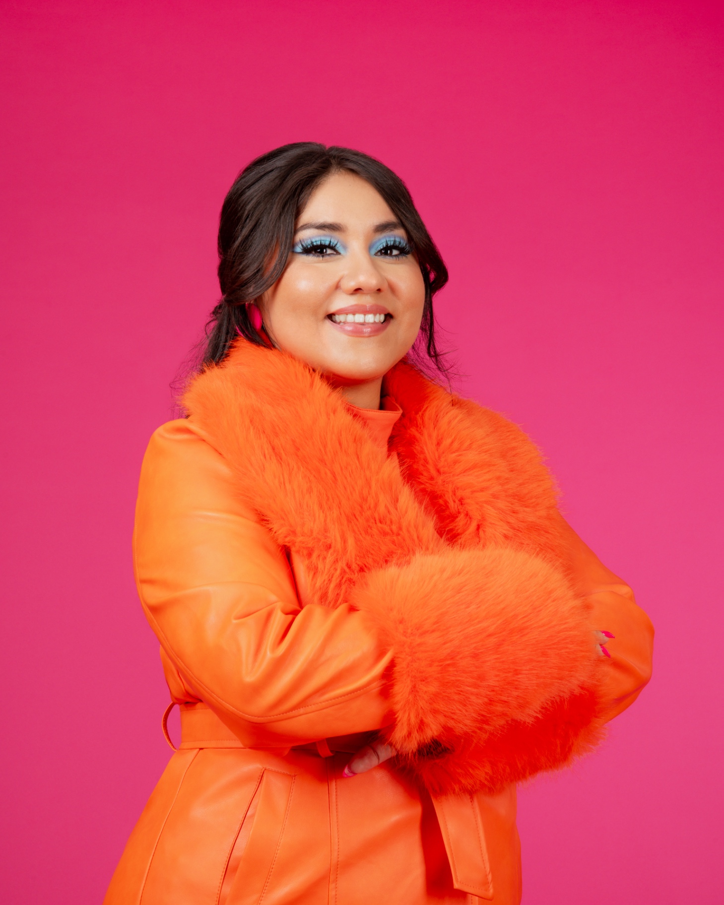 Glo V., educator and consultant, in an orange coat against a hot pink backdrop